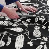 A person cuts a pre-cut fabric featuring a playful, black and white food pattern, ideal for sewing projects like aprons, curtains, or crafts.