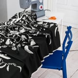 Black fabric with white food patterns under sewing machine, scissors on table, blue chair.