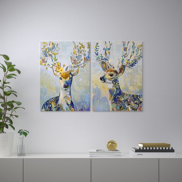 Two vibrant paintings of deer with floral antlers hang on a wall above a grey shelf. The shelf holds various decorative items.
