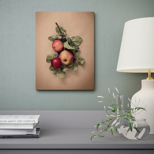 A canvas wall art featuring apples hangs above a shelves with books, a lamp, and a vase with greenery. The deep frame creates a 3d effect.
