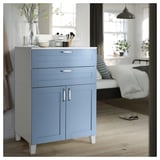 Modern blue storage cabinet with drawers, doors, and white legs, decorated with a vase and items on top, in a cozy room with a bed.