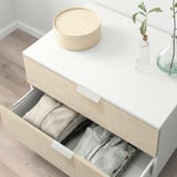 White PLATSA dresser shows open drawer filled with folded clothes, stacked wooden discs atop.
