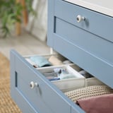 Open blue PLATSA drawer showing organized socks and sweaters in compartments on a wooden floor.