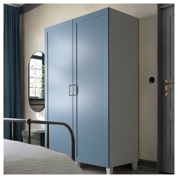 Blue PLATSA wardrobe, modern design, next to bed, light grey walls, gold door handles, mirror and window.