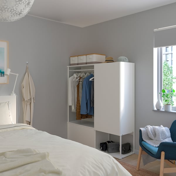 A modern bedroom with a white PLATSA unit, cozy bed, and a blue chair by a large window.