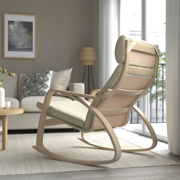 Modern rocking chair with cushions near window; light wood frame, beige cushions.