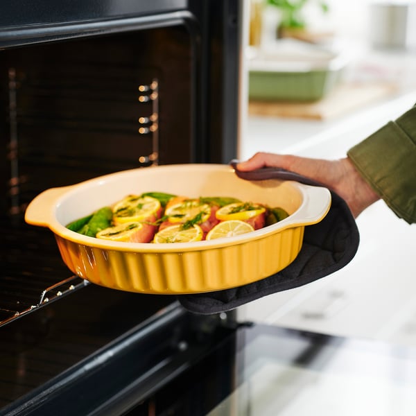 Person holding yellow baking dish with vegetables and lemon slices, ready to be placed in the oven.