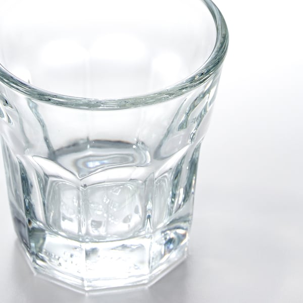 A clear, pristine glass cup sits on a white surface, featuring a diamond-cut texture around its body for a classic, elegant look.
