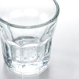 A clear, pristine glass cup sits on a white surface, featuring a diamond-cut texture around its body for a classic, elegant look.