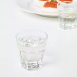 Two glasses with ice sit on a white table, beside a plate with food.