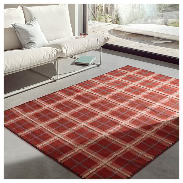 Modern living room with white sofa, red tartan rug, concrete floor, and large window.