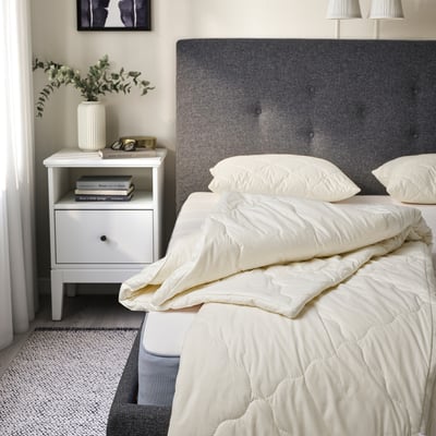 Minimalist bedroom with gray duvet, two white pillows, gray headboard, nightstand, and floral vase.