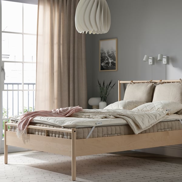 Cozy bedroom with light wooden bed, large windows, minimalist design, neat bedding.