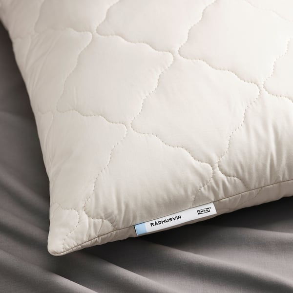 A close-up of a white quilted pillow on bedding, labeled RÅDHUSVIN.