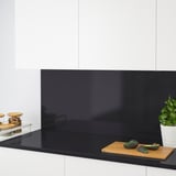Minimalist kitchen with a black quartz countertop and backsplash, wooden cutting board, avocados, and jars.