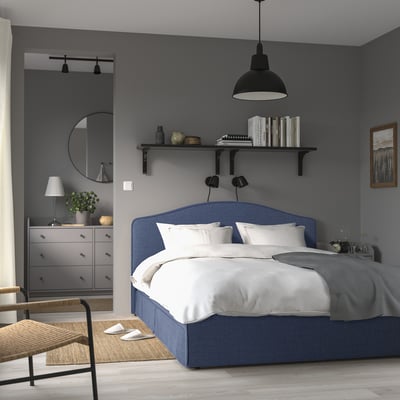 Elegant grey bedroom with large, blue RAMNEFJÄLL bed. Upholstered headboard, white linens, modern decor.