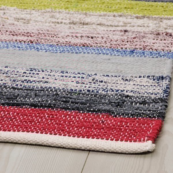 Colorful, handwoven cotton rug displayed on a wooden floor, showcasing a mix of vibrant and neutral stripes.