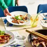 Plant-based meal with sausages, veggies, dip, and drink. Person serving.