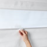 A hand adjusts white RINGBLOMMA roman blind, showing its light-filtering fabric and cordless raising mechanism.