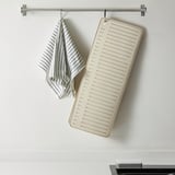 Kitchen mat hangs from wall, striped cloth underneath. Efficient drying with ridges.