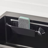 Black sink caddy with green sponge and scrub brush, showing organized storage near sink.