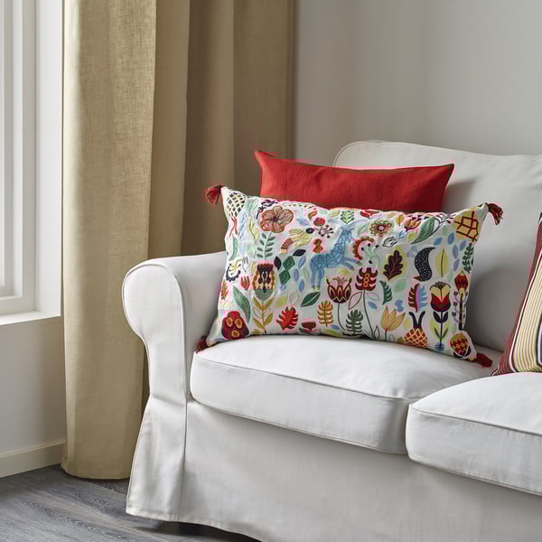 A white sofa with a vibrant, colorful floral pillow featuring tassels and a solid red pillow, emphasizing comfort and decorative appeal.