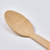 Close-up of a well-crafted bamboo spoon on a plain background, displays smooth texture and natural grain.