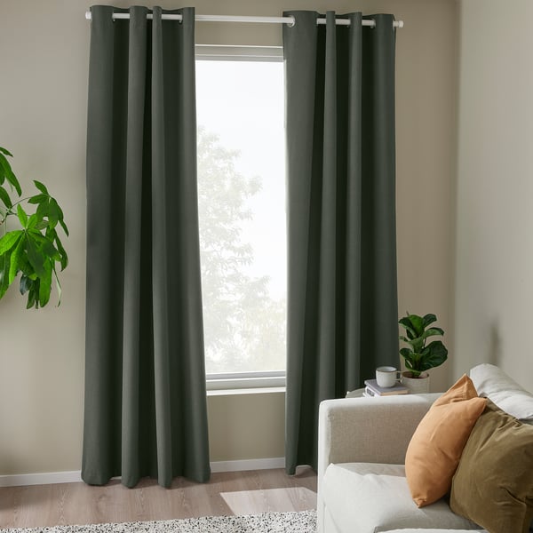 Dark green block-out curtains with eyelets frame large window, complementing cozy beige couch and adding a peaceful ambiance to the room.