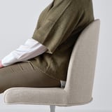 Person sitting on a gray, upholstered, swivel chair, leaning back with arms resting on chairs curve.