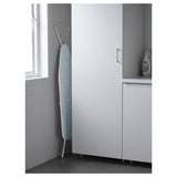 An ironing board set up in a corner, made of steel, with adjustable height. A steam generator is visible.