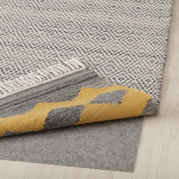 Gray patterned rug with yellow border, folded back to show felt backing.