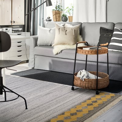 Modern living room with gray RYSSGRÄS rug, comfortable sectional, and woven basket trolley.