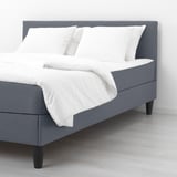 A gray upholstered bed with a padded headboard, featuring white bedding and four pillows, offering comfort for sleeping and reading.