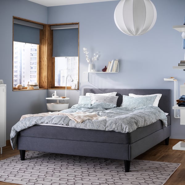 Modern bedroom with gray SÄBÖVIK bed, blue walls, white pendant light, wooden floor, and city view window.