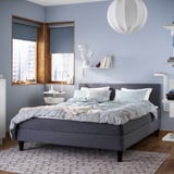 Modern bedroom with gray SÄBÖVIK bed, blue walls, white pendant light, wooden floor, and city view window.