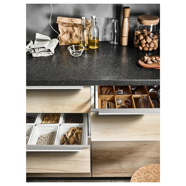 Wooden kitchen setup with open drawers showing food items and cooking tools, dark countertop with bottle and utensils.