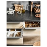Wooden kitchen setup with open drawers showing food items and cooking tools, dark countertop with bottle and utensils.