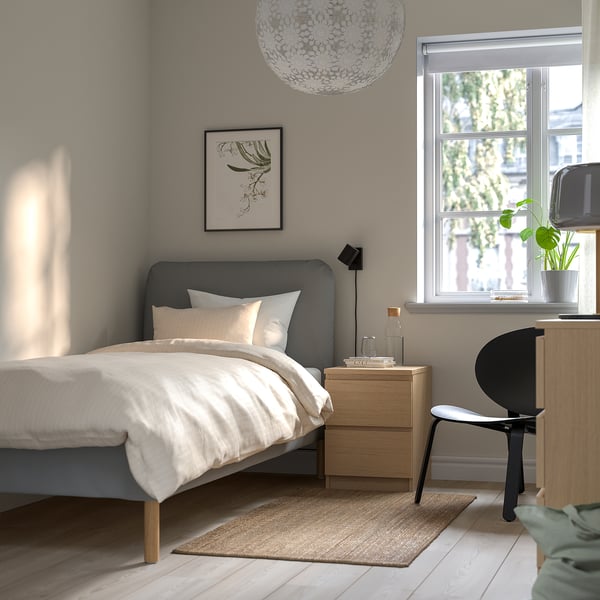 Modern bedroom with SAGESUND bed, pillows, nightstand, lamp, plants, chair, desk, jute rug.