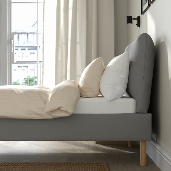 Modern bed frame with sloped headboard and pillows by window, offering comfort and style.