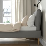 Modern bed frame with sloped headboard and pillows by window, offering comfort and style.