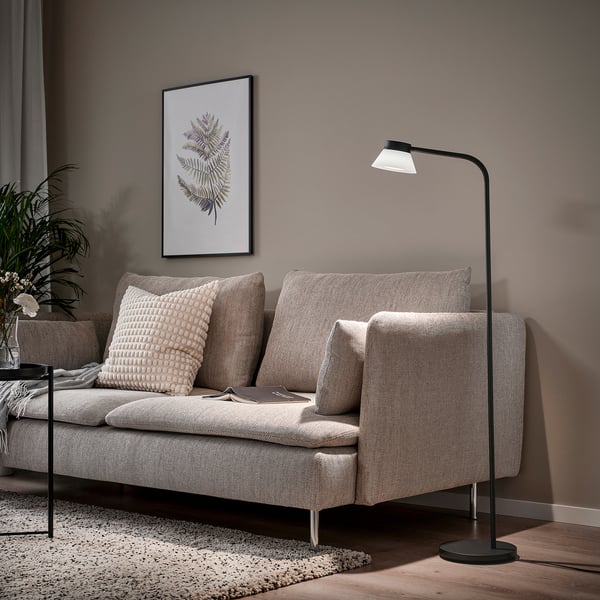 Modern living room with SAMBORD floor lamp, beige sofa, and plant poster. Lamp beside sofa provides reading light.