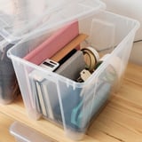 Clear plastic storage box with lid, containing school supplies like rulers, calculators, and notebooks. The lid has a built-in click lock function.