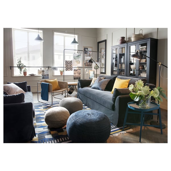 Modern living room with grey sofa, yellow pillows, blue rug, plants, and large windows.