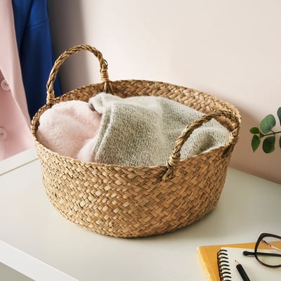 A SANDJORD woven basket in natural tones holding pink and white items. Its medium-sized, suitable for desk use.