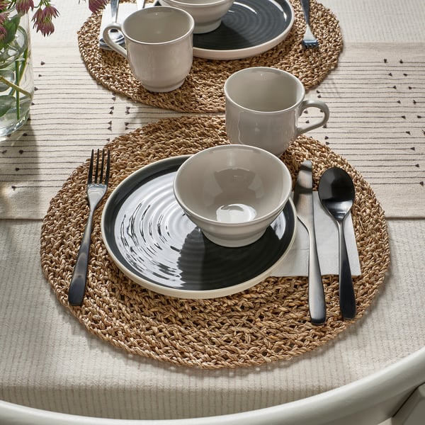 Rustic table setting with gray plates, bowls, and mugs on woven placemats, featuring cutlery, ready for dining.
