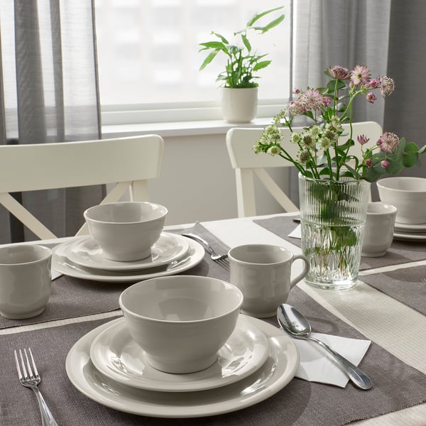 Table set with white ceramic dinnerware, floral vase, and outdoor view.