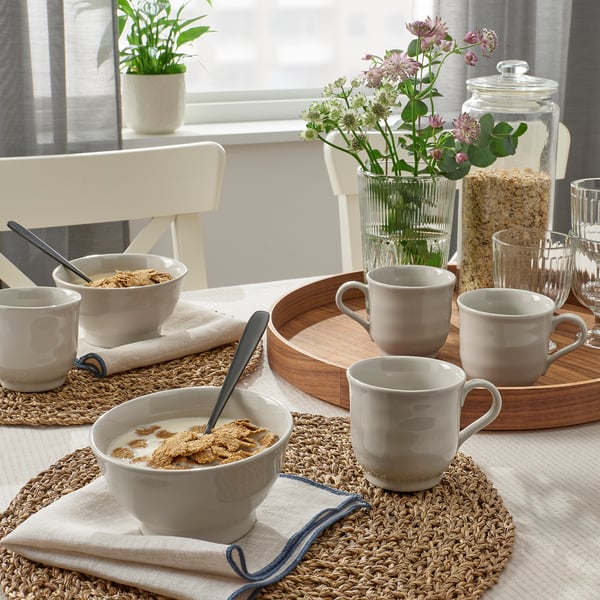 A cozy dining setup with bowls of cereal, mugs, and flowers on a rustic wooden tray.
