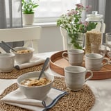 A cozy dining setup with bowls of cereal, mugs, and flowers on a rustic wooden tray.