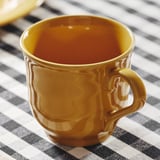 Gold mug on striped tablecloth, smooth surface, robust design.