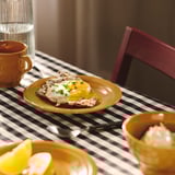 Yellow plate with fried egg and herbs. Surrounded by cups and glasses on a checkered tablecloth.
